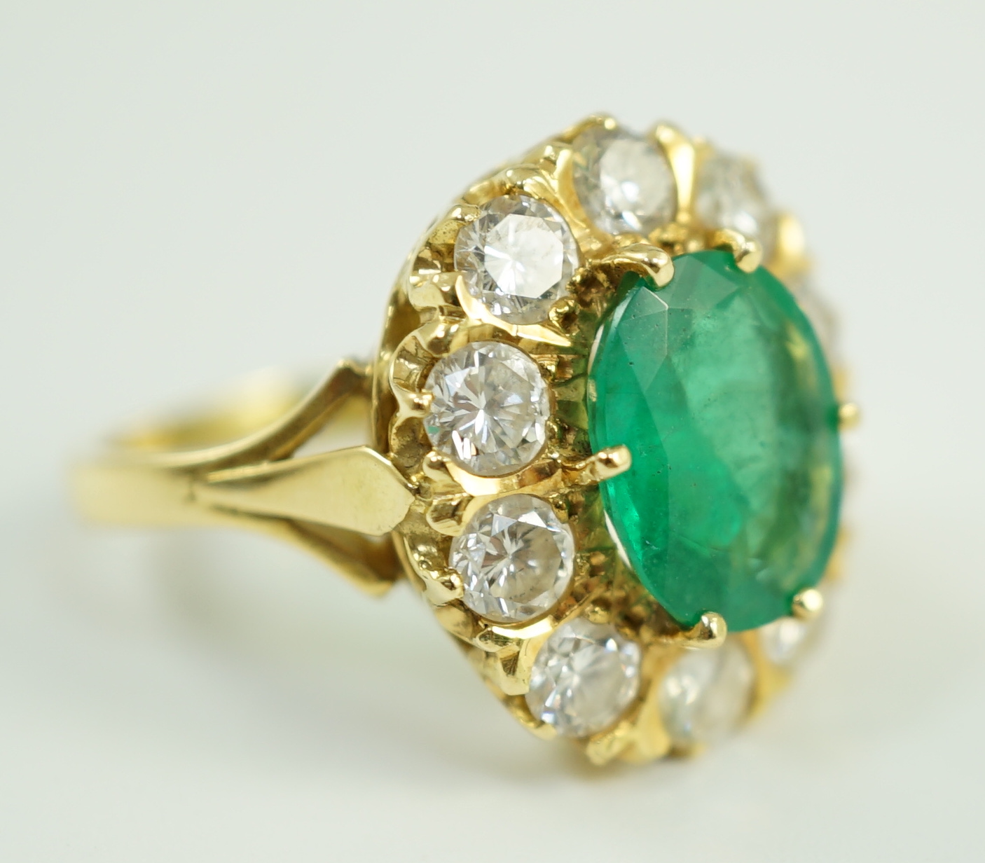 A modern 18ct gold, emerald and diamond set oval cluster ring